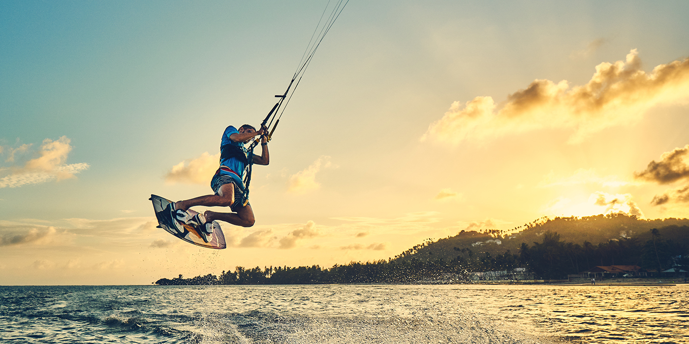 Young man kite boarder jumps over the sea at sunset