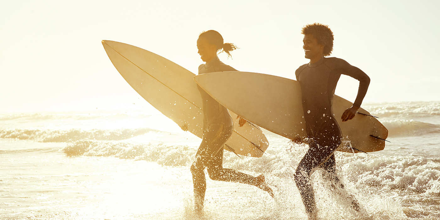 Sunset, running and couple on the beach with surfboards to practice surfing while on vacation. Nature, sports and young man and woman surfers in the ocean or sea while on a tropical holiday in Hawaii