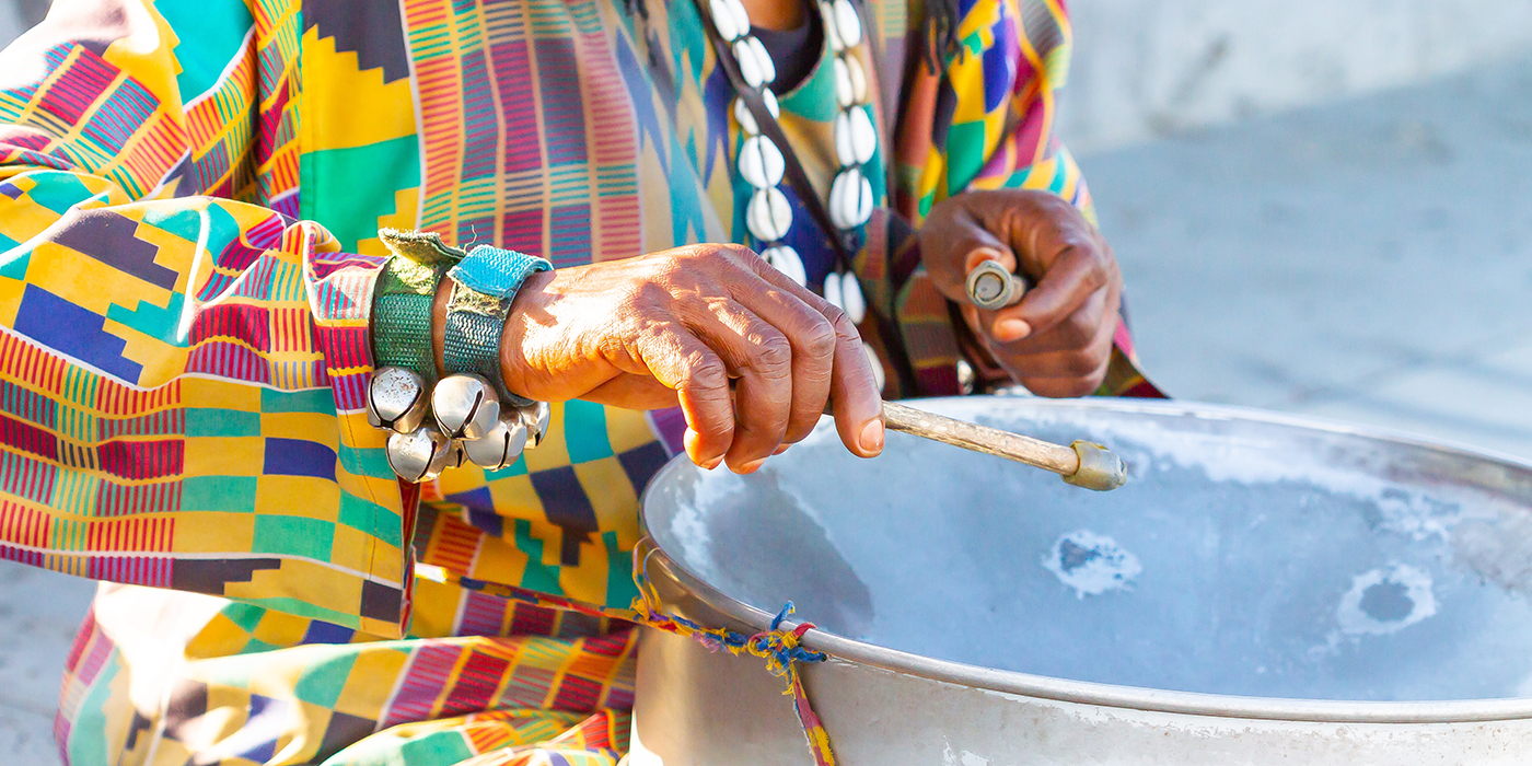 African musician seated in colorful dress playing musical instru